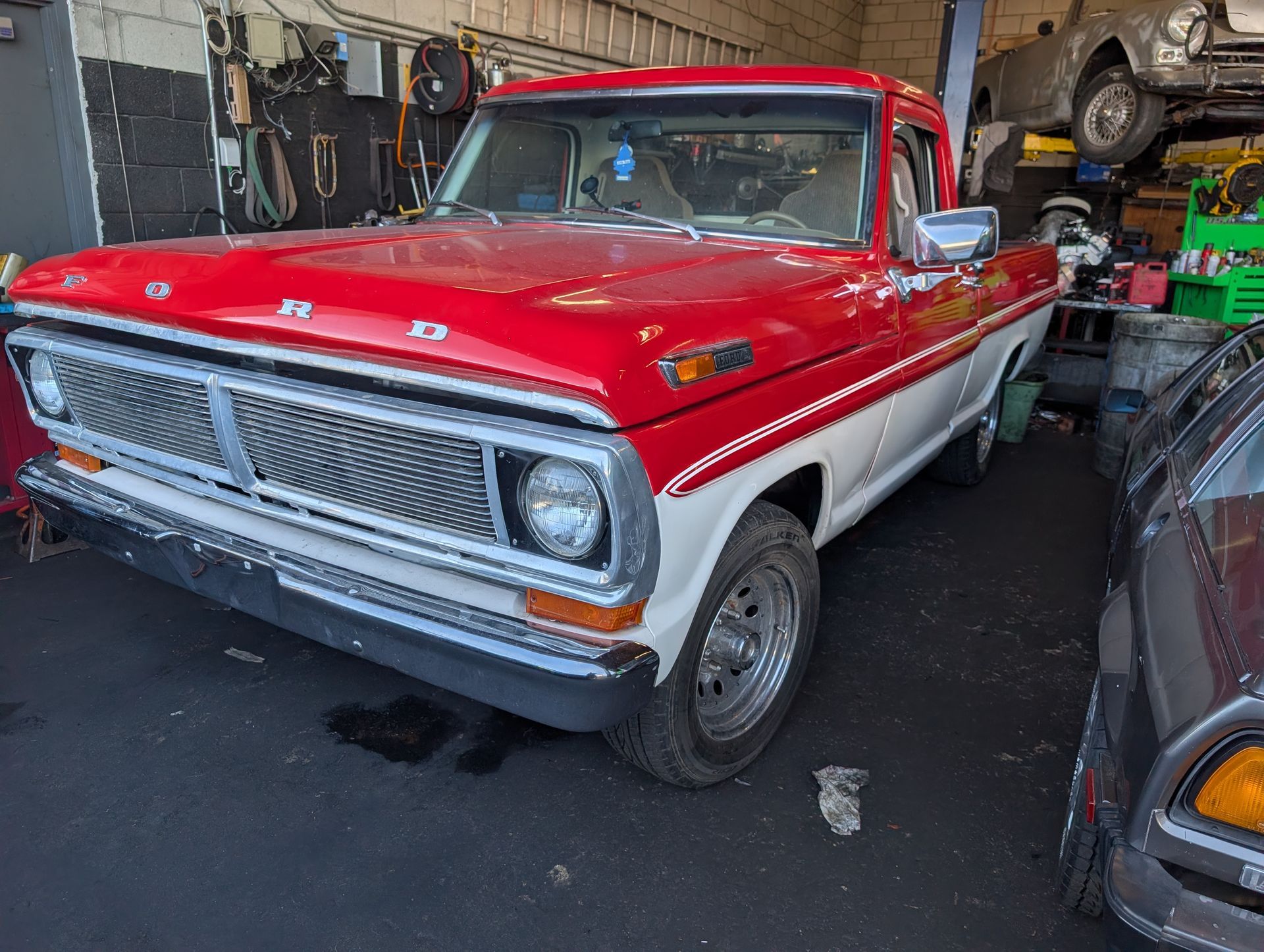 Red classic pickup truck parked in a garage, front view with chrome grille and white lower body panels
