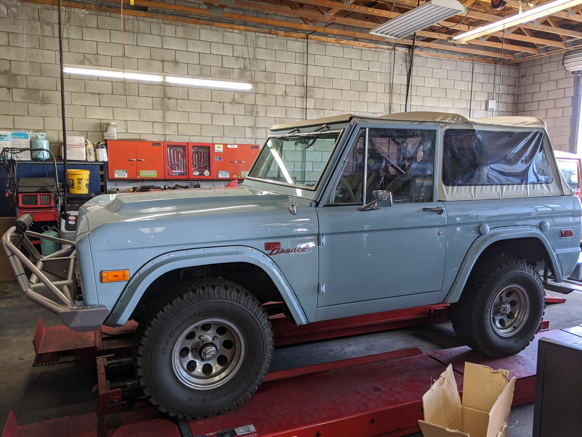 Light blue vintage off-road SUV in a garage on a red lift, with tools and boxes nearby