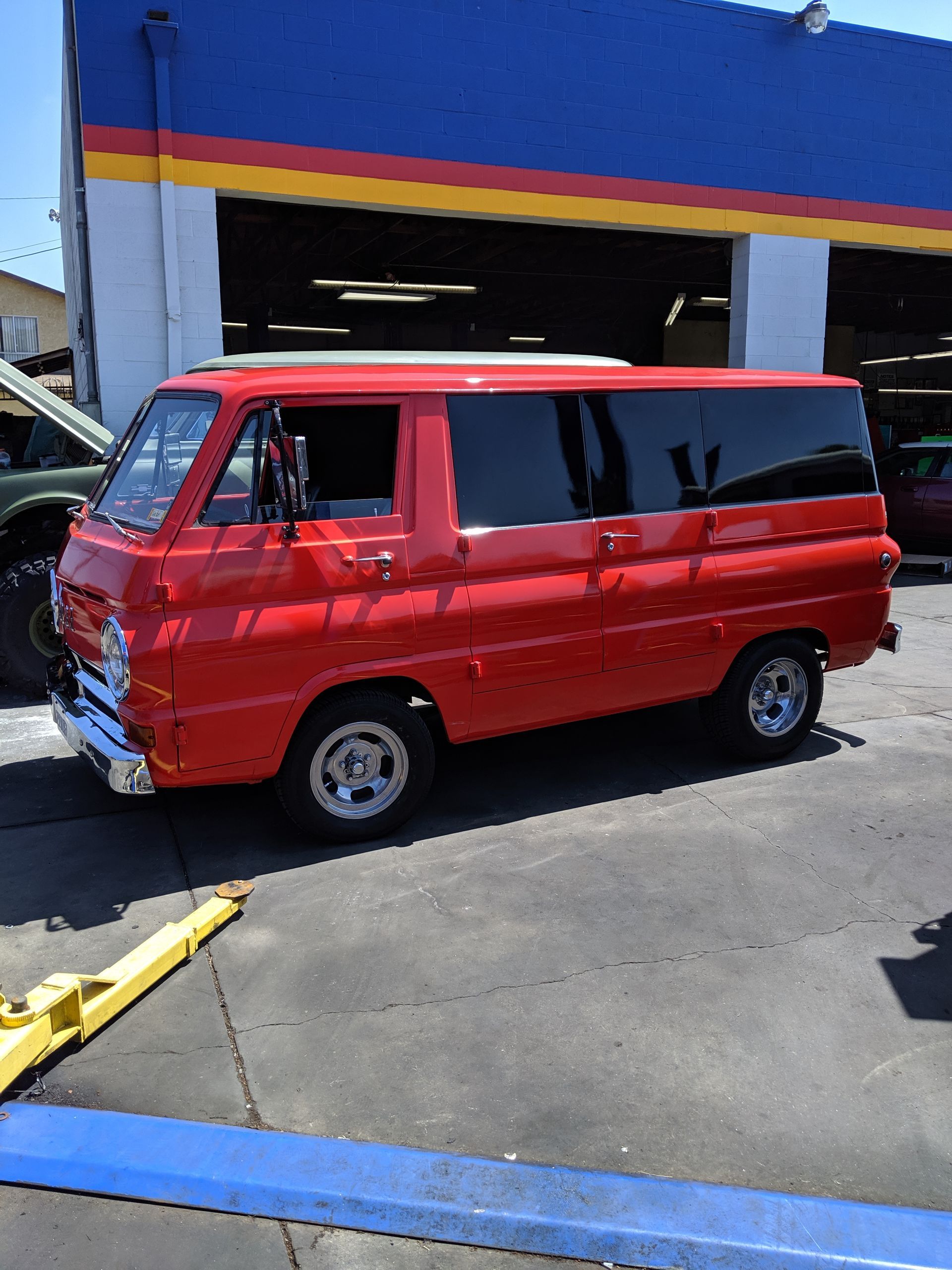 Red vintage van parked outside an auto shop with a blue-and-yellow facade