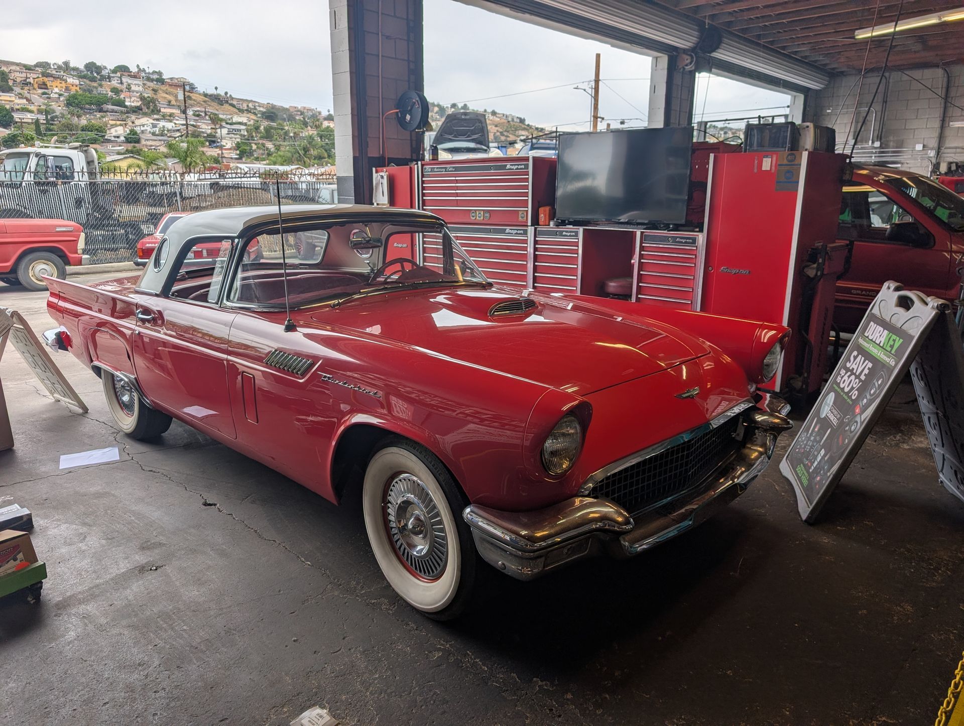 Red vintage convertible car in a garage, with open hood and a tool chest nearby.