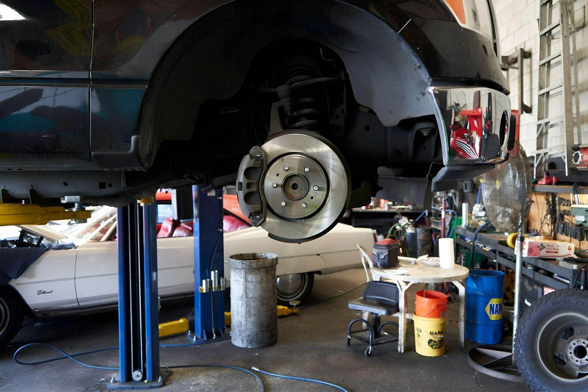 Car lifted in an auto shop, exposing the rear brake and wheel hub during repair.
