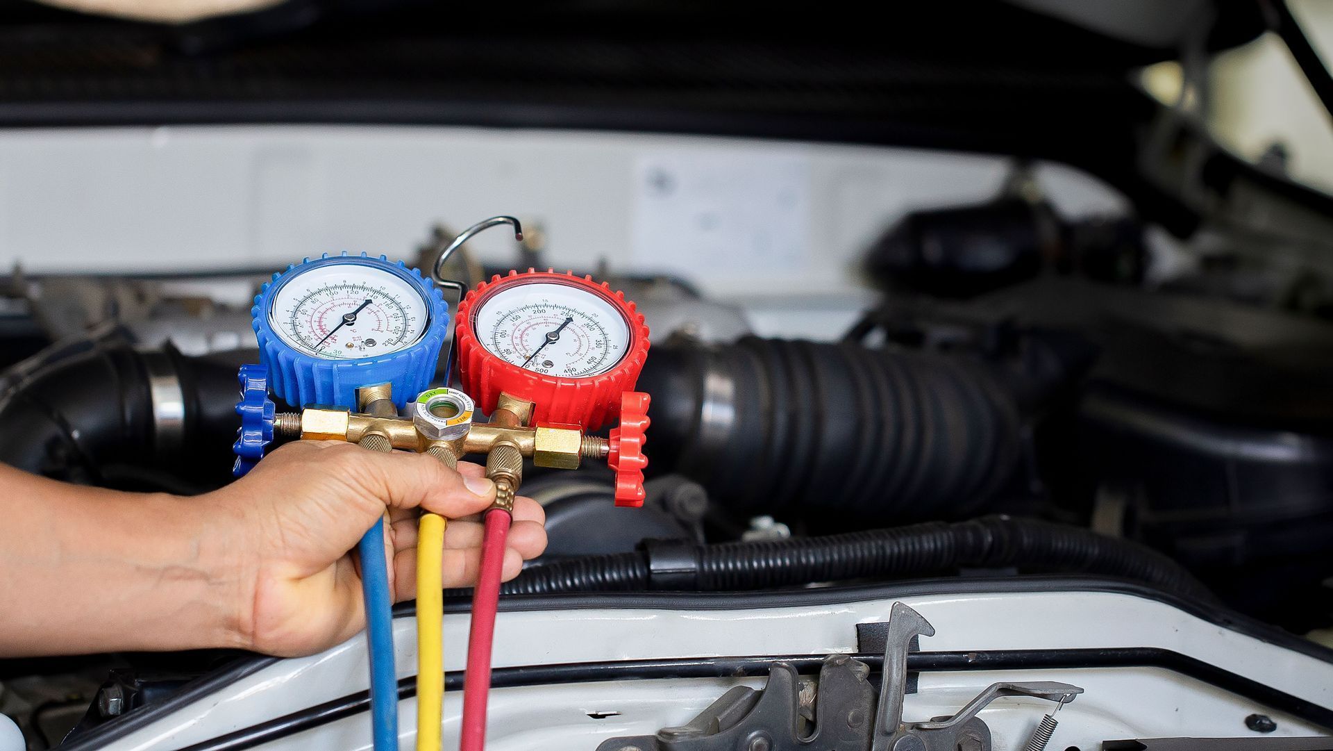 Hand holding red and blue HVAC manifold gauges in front of a car engine bay