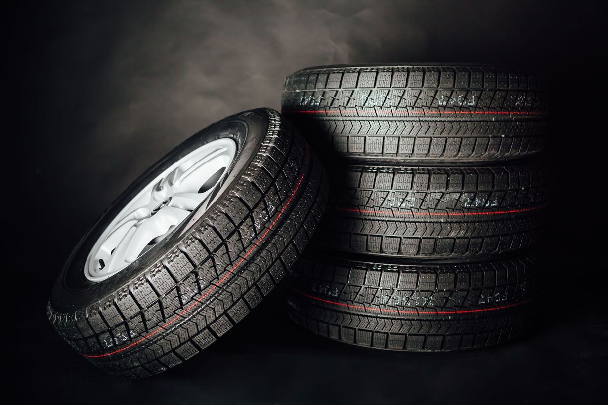 Stack of black car tires beside one upright tire with a silver rim on a dark background
