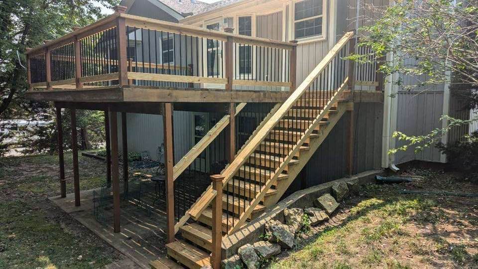 A wooden deck with stairs leading up to it is in the backyard of a house.