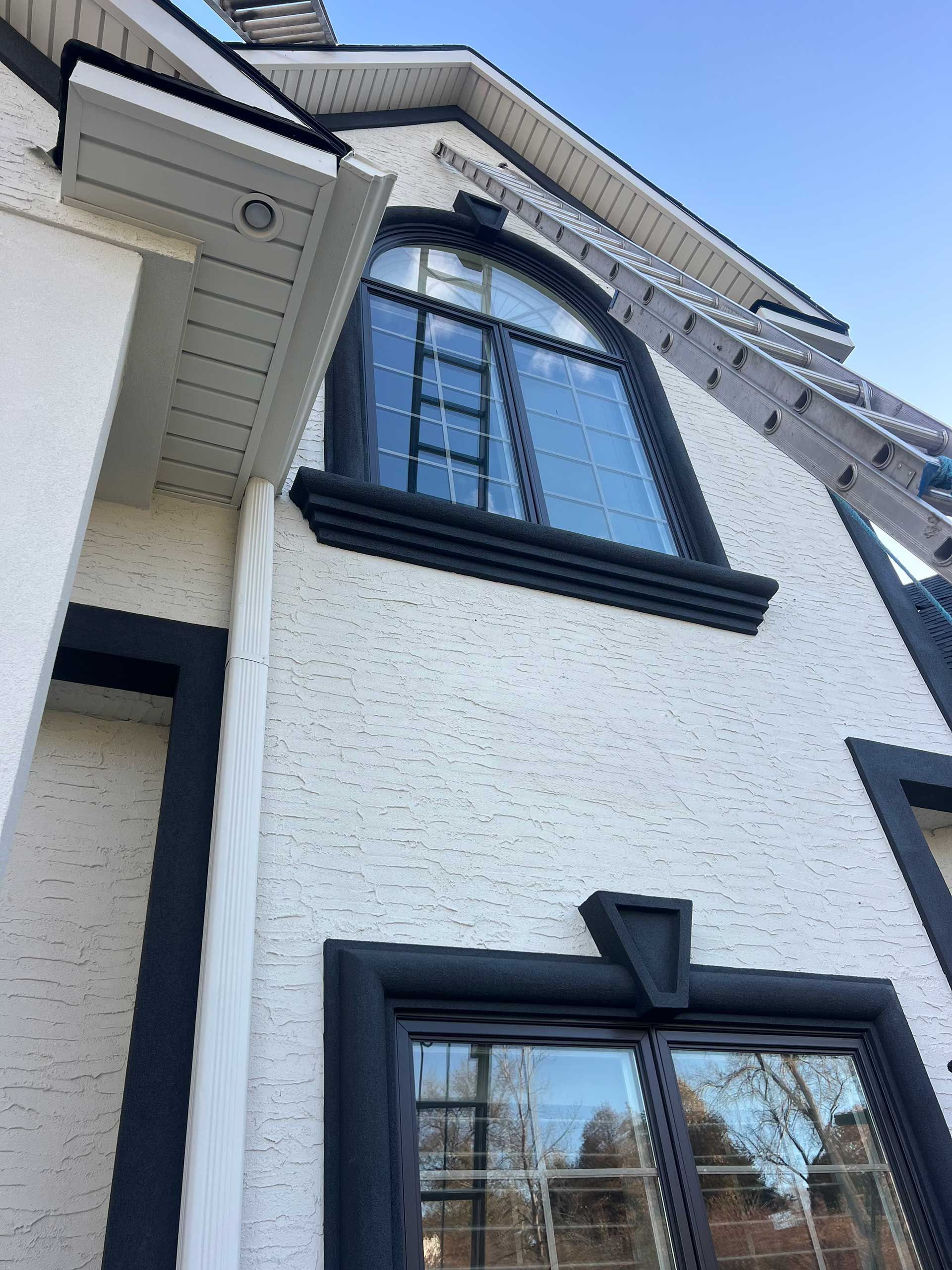 white stucco house with black trim, arched window, and ladder against the side