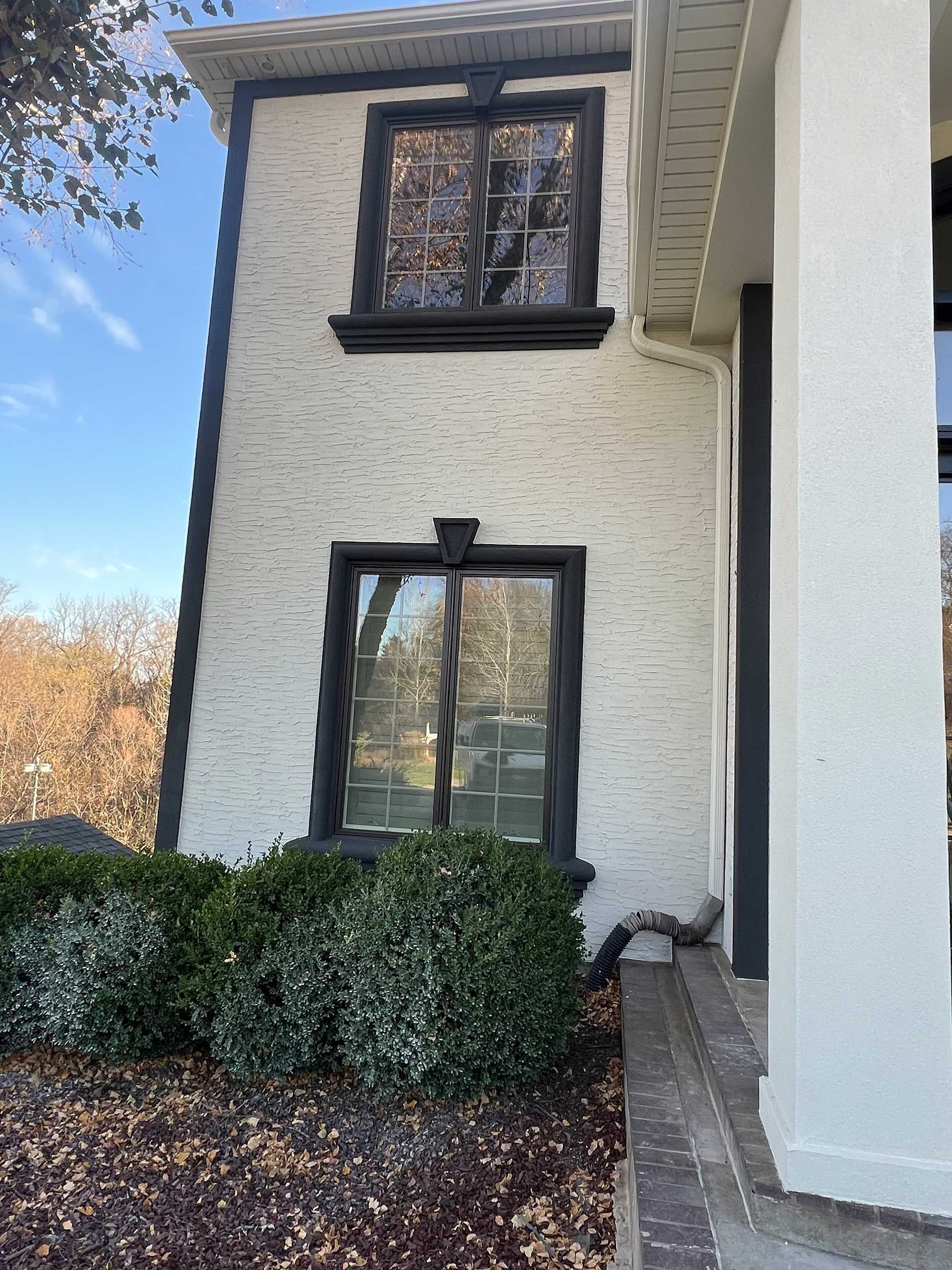 white brick building with black trim around windows and edges, bush in front