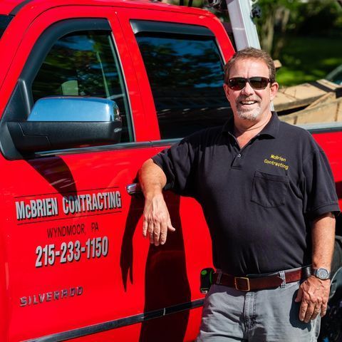 A man is leaning against a red mcbrien contracting truck