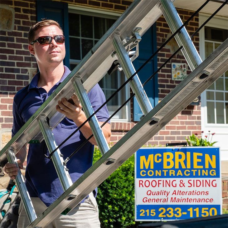 A man carrying a ladder in front of a mcbrien contracting sign