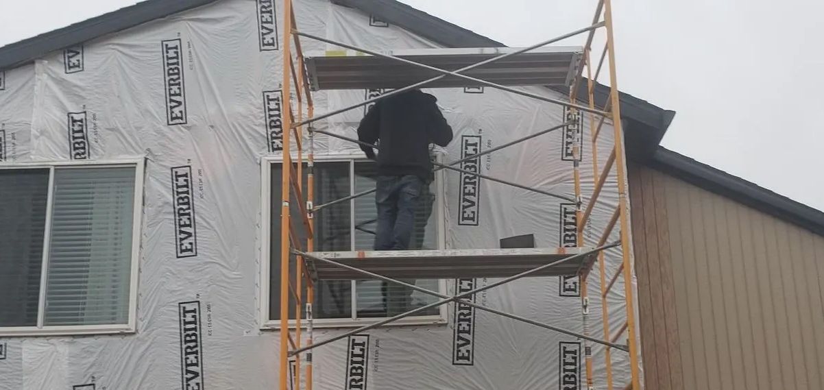 Worker on scaffolding installing siding on a house under construction.