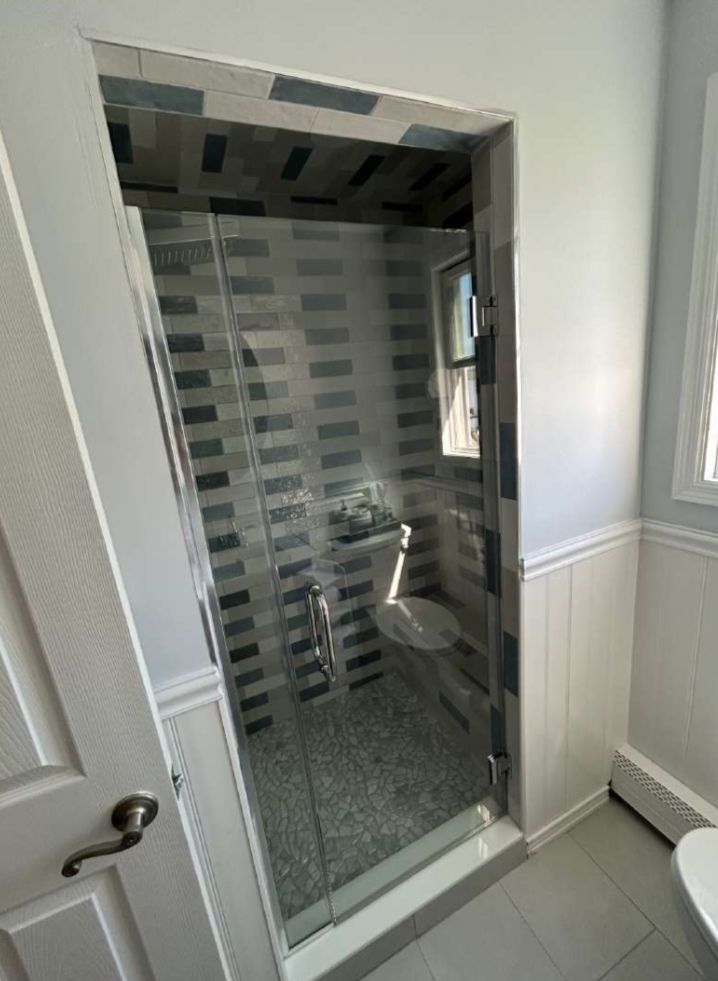 Bathroom with glass shower door, gray tiled walls, and white trim.
