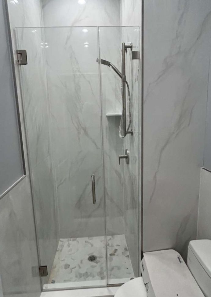 Glass shower enclosure with white marble-look tile walls, chrome shower fixtures, and a white tile base.