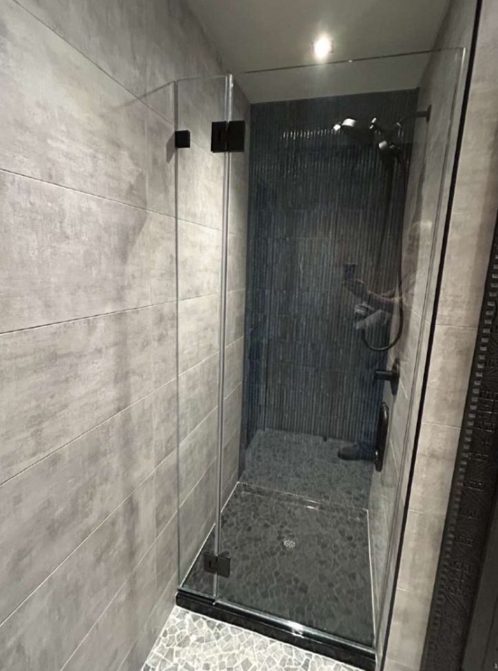 Shower stall with grey tile walls, a glass door, and dark fixtures.
