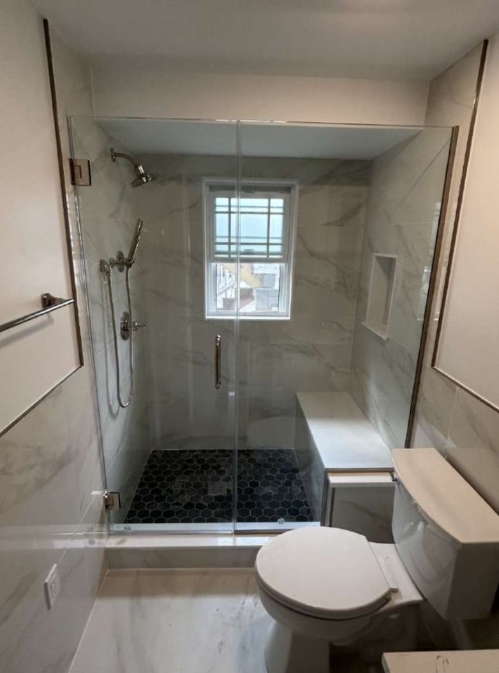 Bathroom with glass shower, marble walls, dark pebble floor, built-in bench, and white toilet.