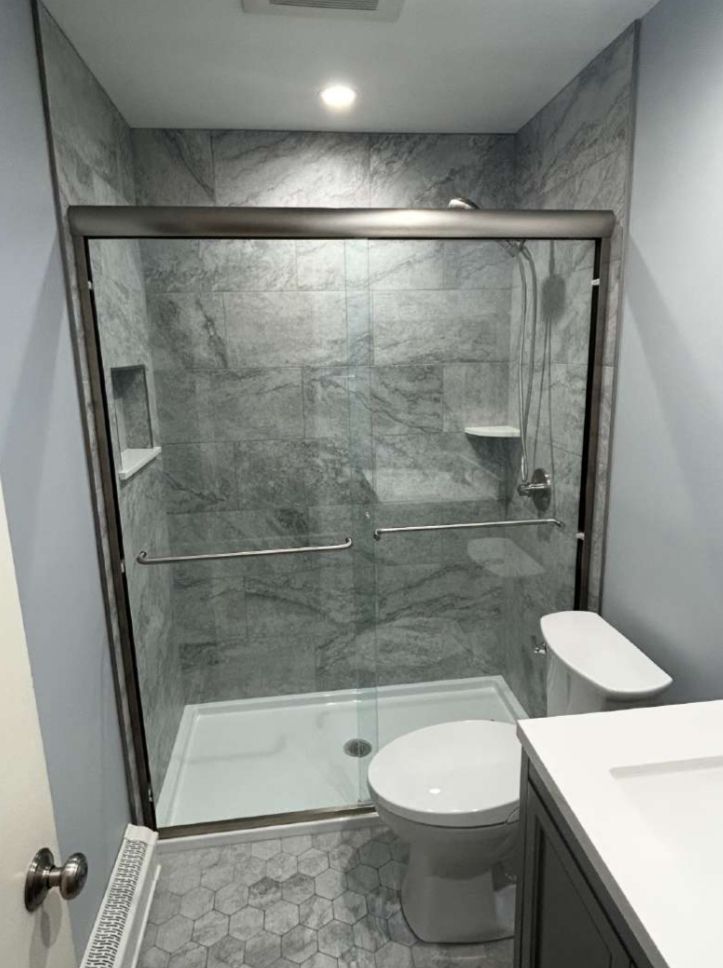 Modern bathroom with gray tiled shower, glass doors, and toilet.