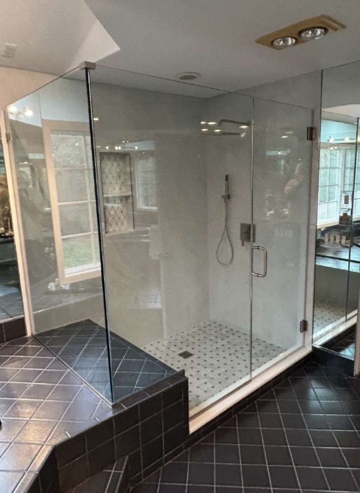 Glass-enclosed shower in a modern bathroom with black tile floor and small white and black mosaic shower floor.