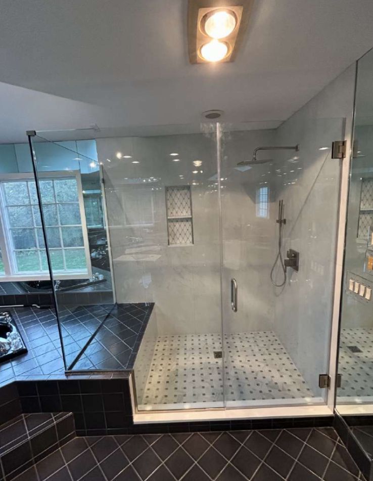 Glass-enclosed shower with black tile floor and built-in bench. White and black patterned floor, shower fixtures.