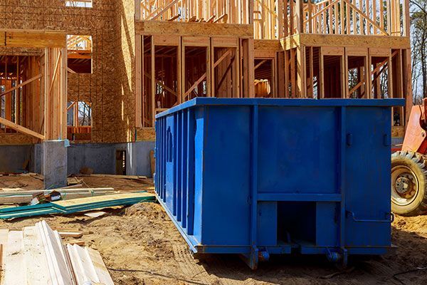 A blue dumpster is parked in front of a house under construction.