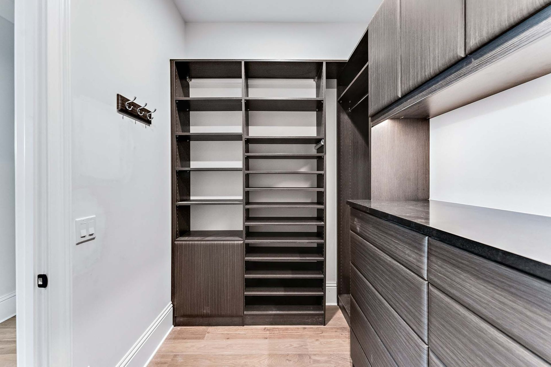 Modern walk-in closet with dark built-in shelving, drawers, and white walls