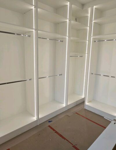 Empty white built-in closet shelves and hanging rods in a room under construction.