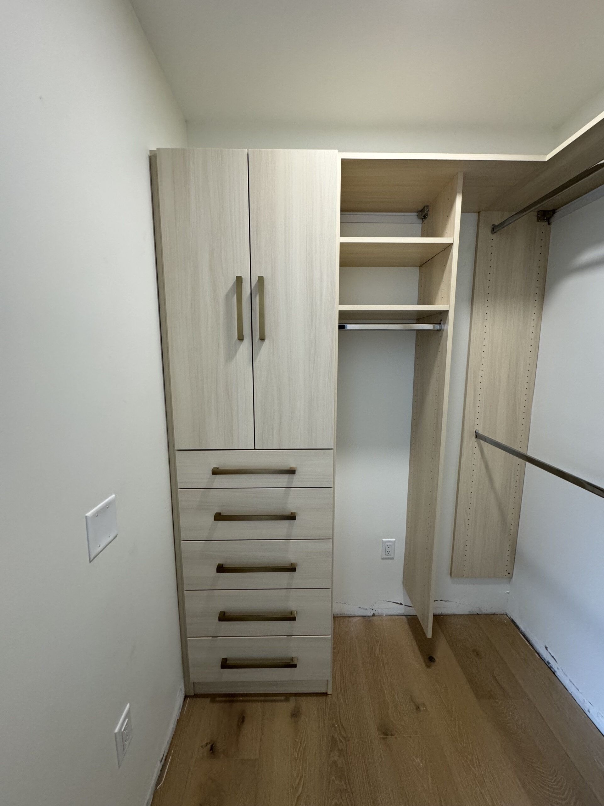 Built-in light wood closet with drawers and open shelving in a narrow room with wood flooring