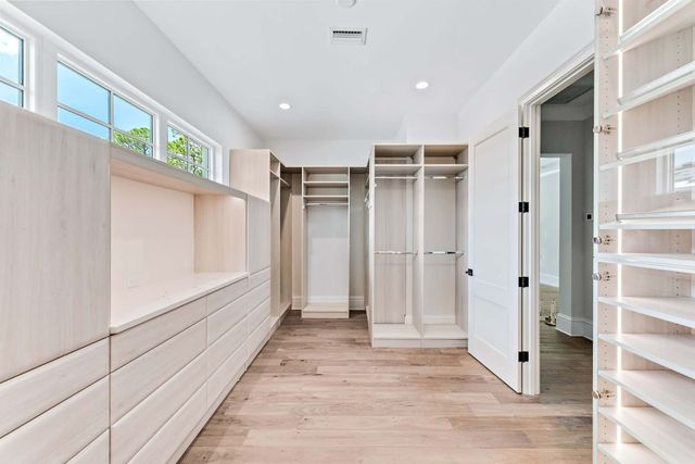 Bright walk-in closet with white shelves, drawers, and hanging space, plus wood flooring and open doors.