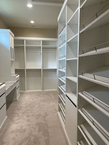 Empty walk-in closet with white shelving and hanging rods, beige carpet, and ceiling lights
