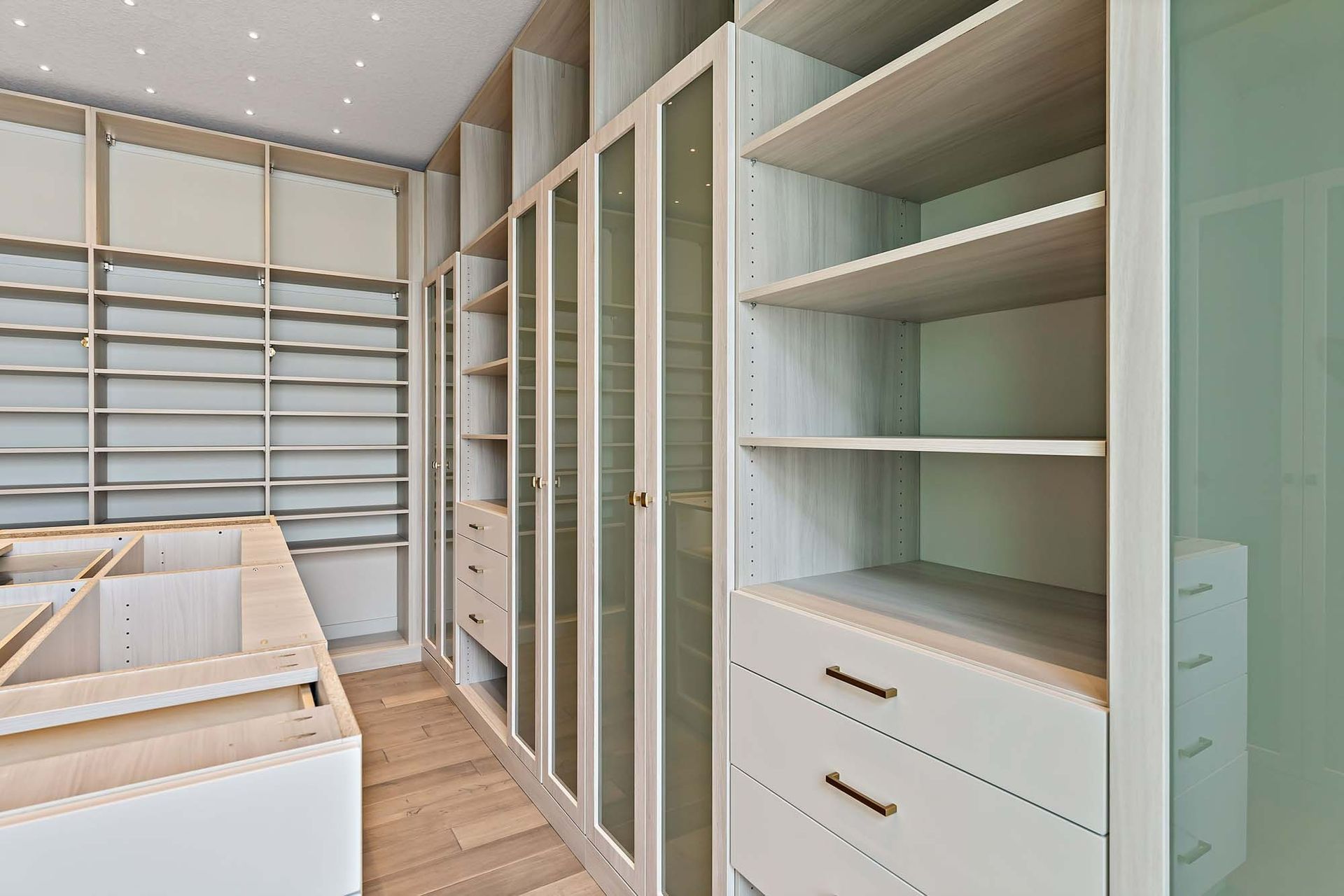 Walk-in closet with white built-in shelves, drawers, and hanging rods in a bright room
