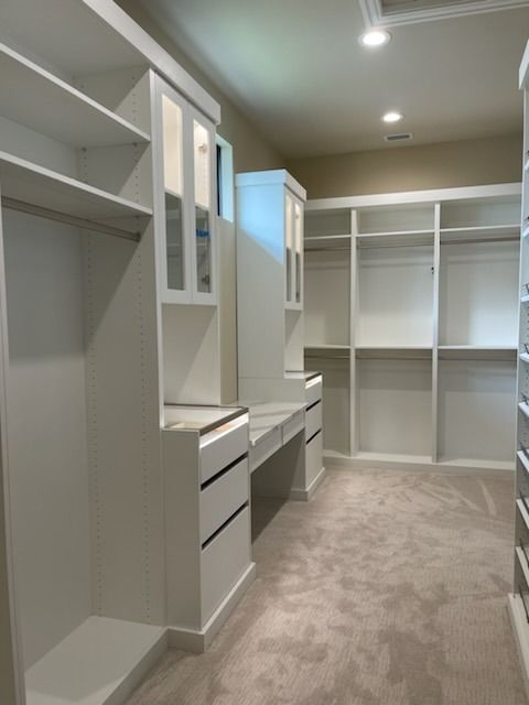 Walk-in closet with white shelving, drawers, and a built-in vanity on beige carpet
