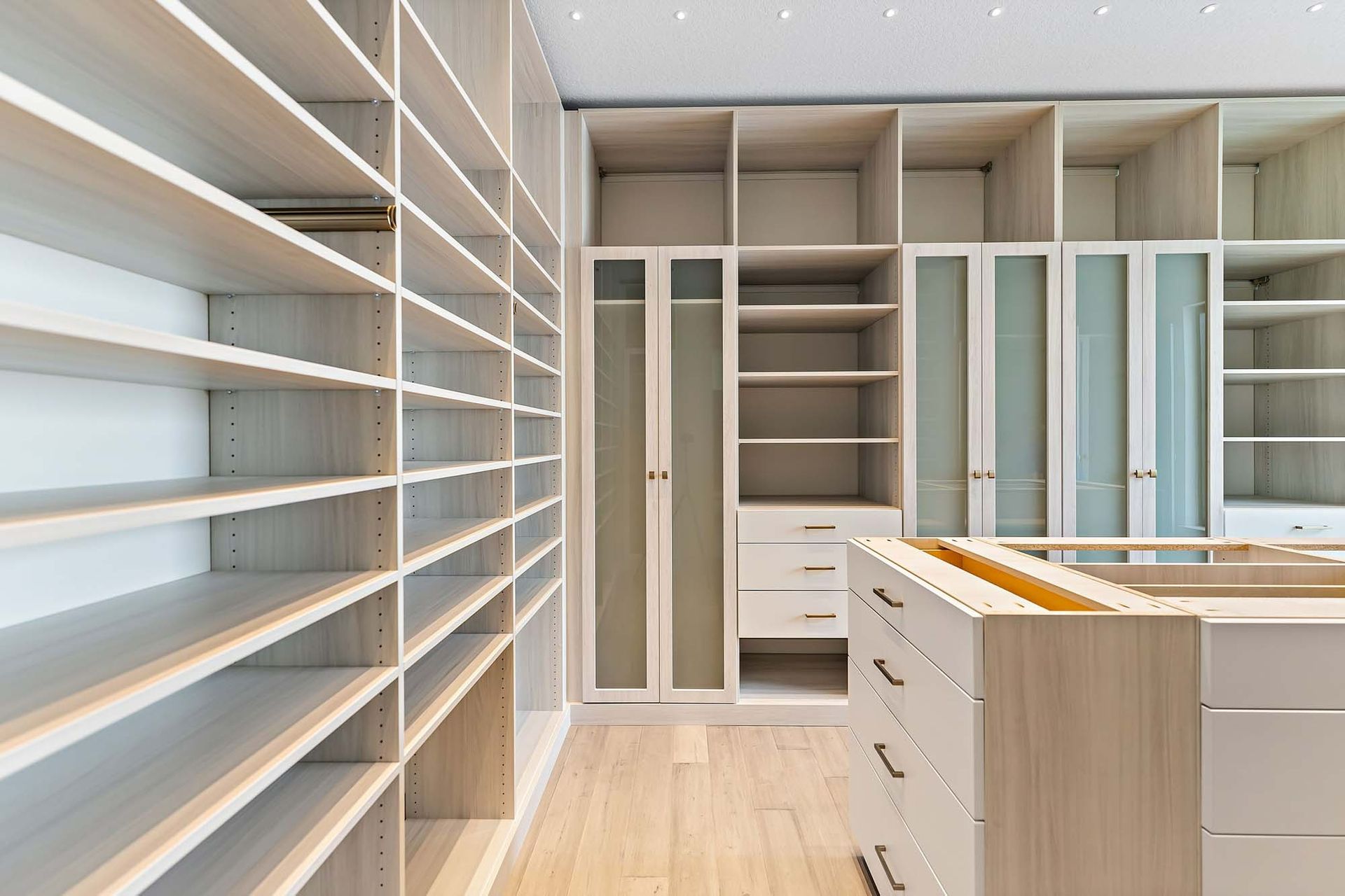 Bright walk-in closet with white shelving, hanging rods, drawers, and light wood floors