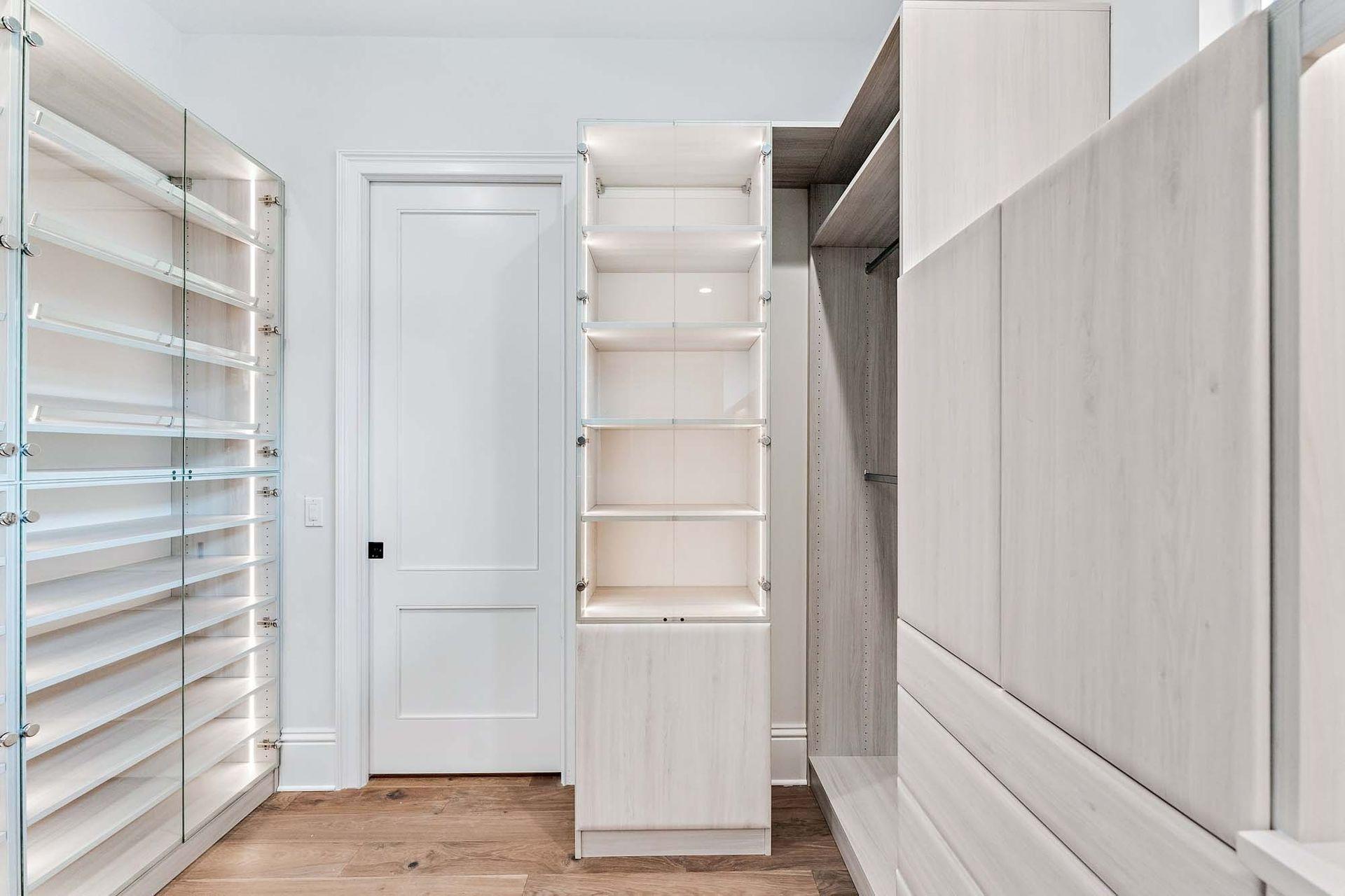 Bright walk-in closet with white shelving, wood floor, and closed white door.