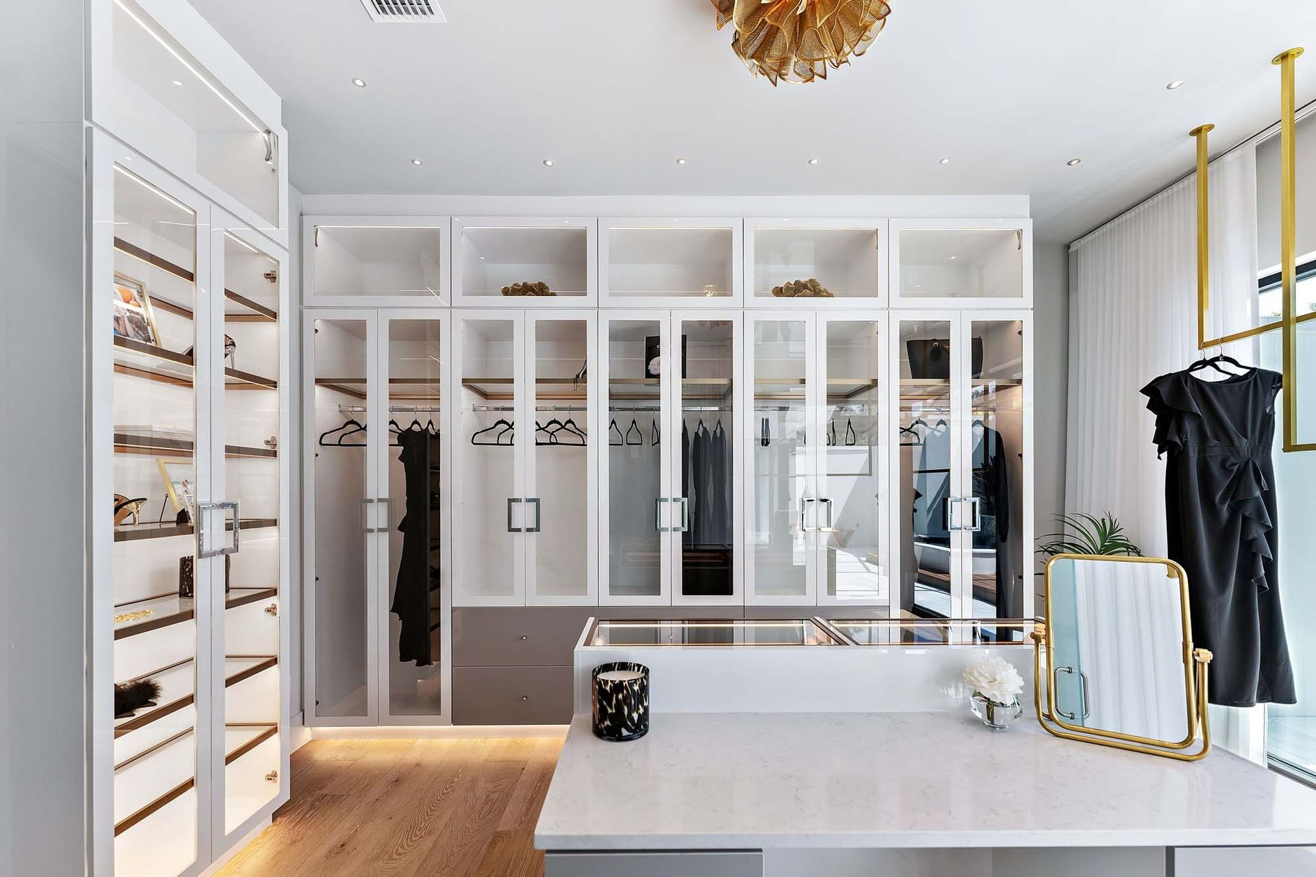 Bright walk-in closet with white built-in shelving, mirrored doors, and clothing racks