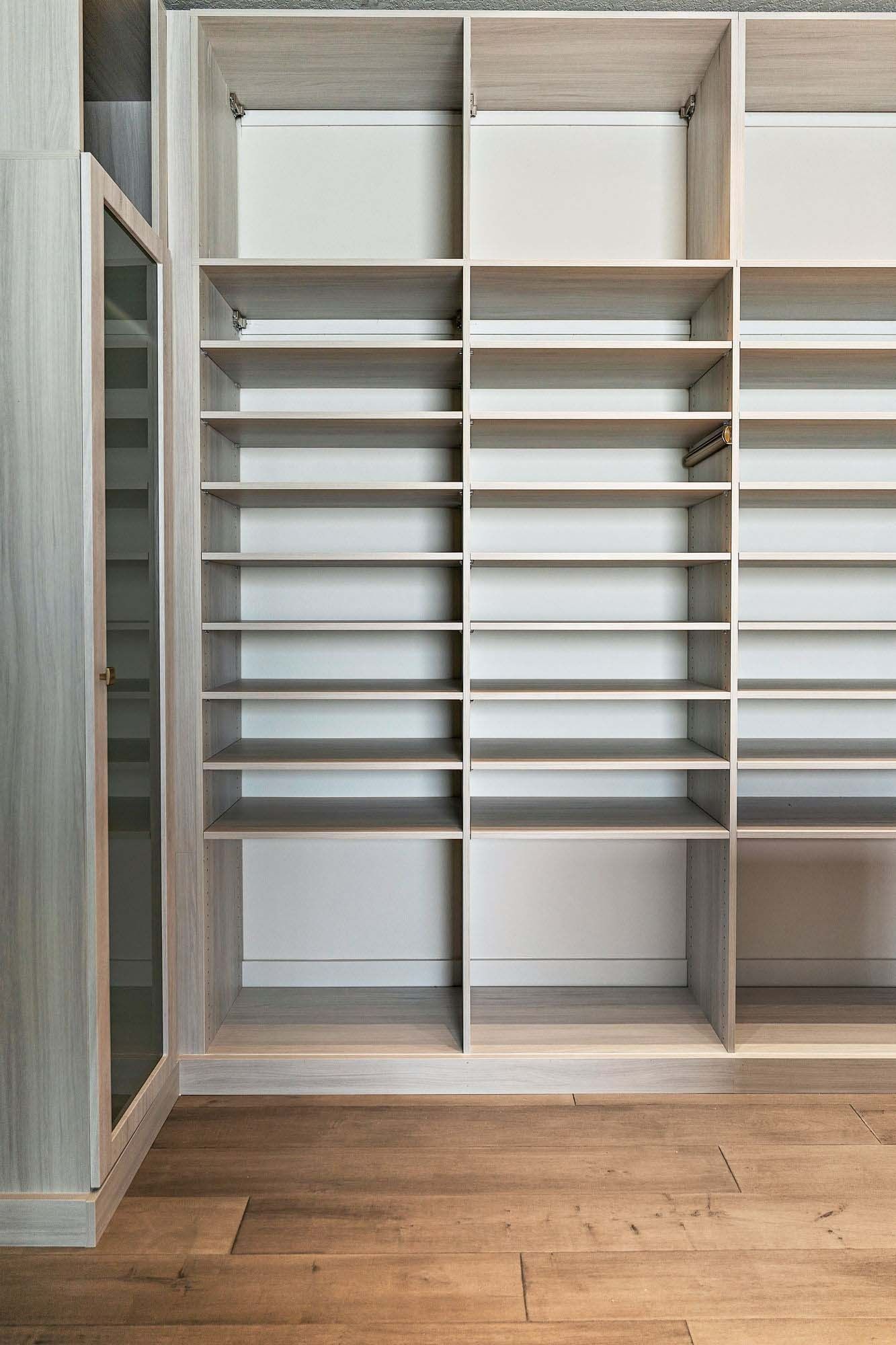 Empty built-in closet with white shelving and sliding shoe racks, wood flooring below