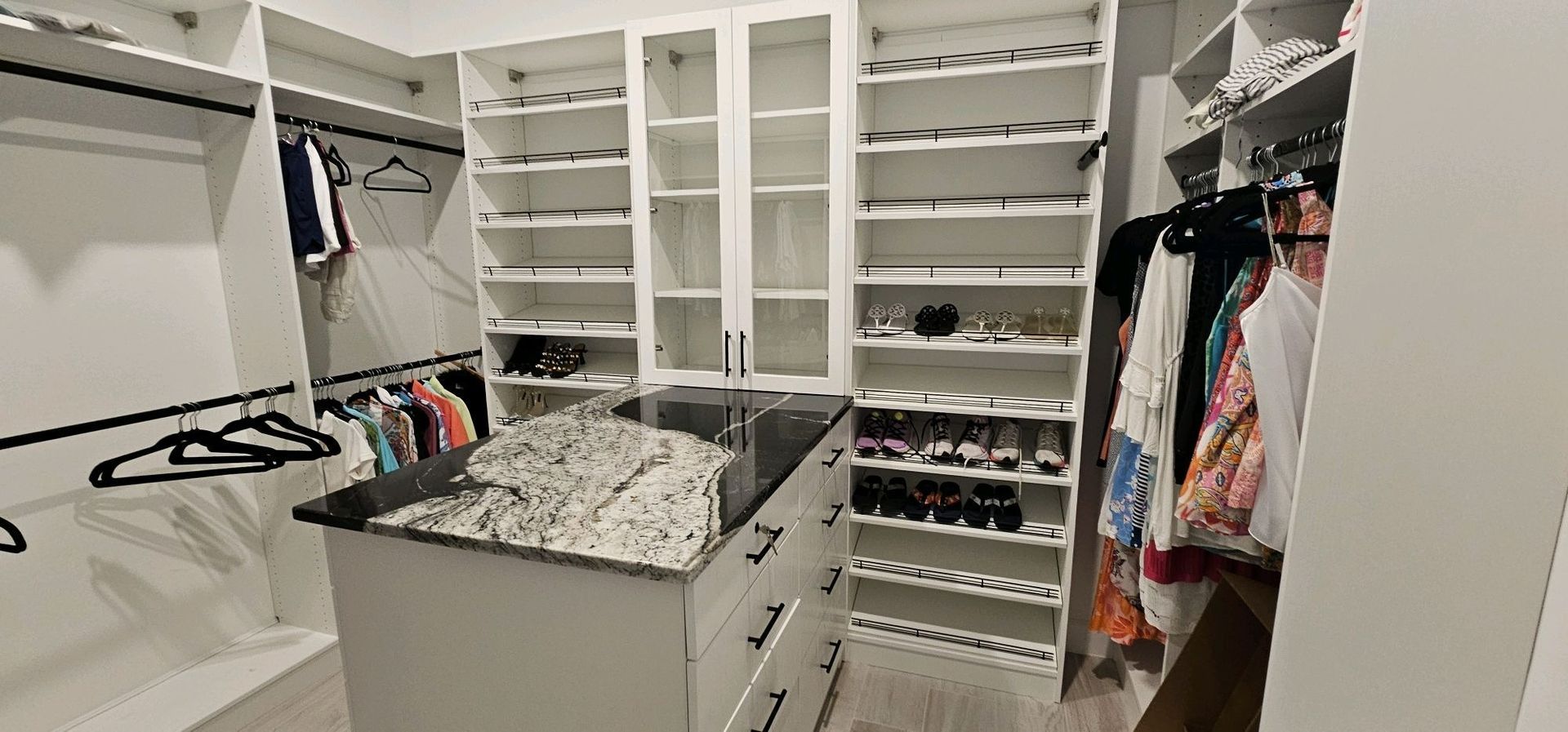 Walk-in closet with shelves, hanging clothes, drawers, and a central island covered in folded items.