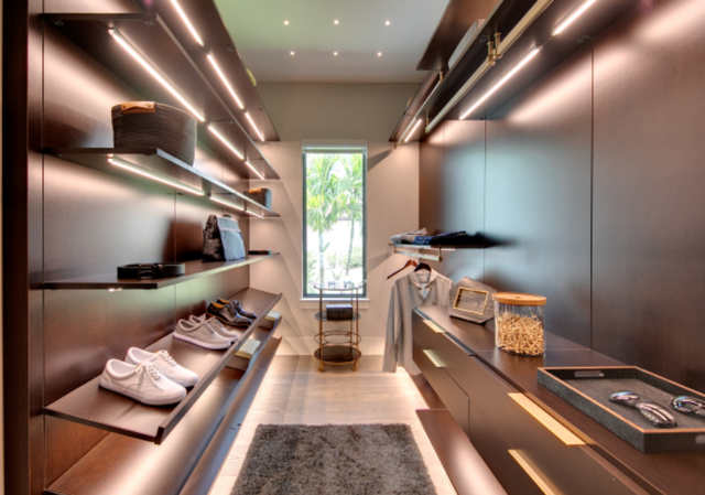 Modern minimalist walk-in closet with shelves, hanging clothes, and a narrow window at the end.
