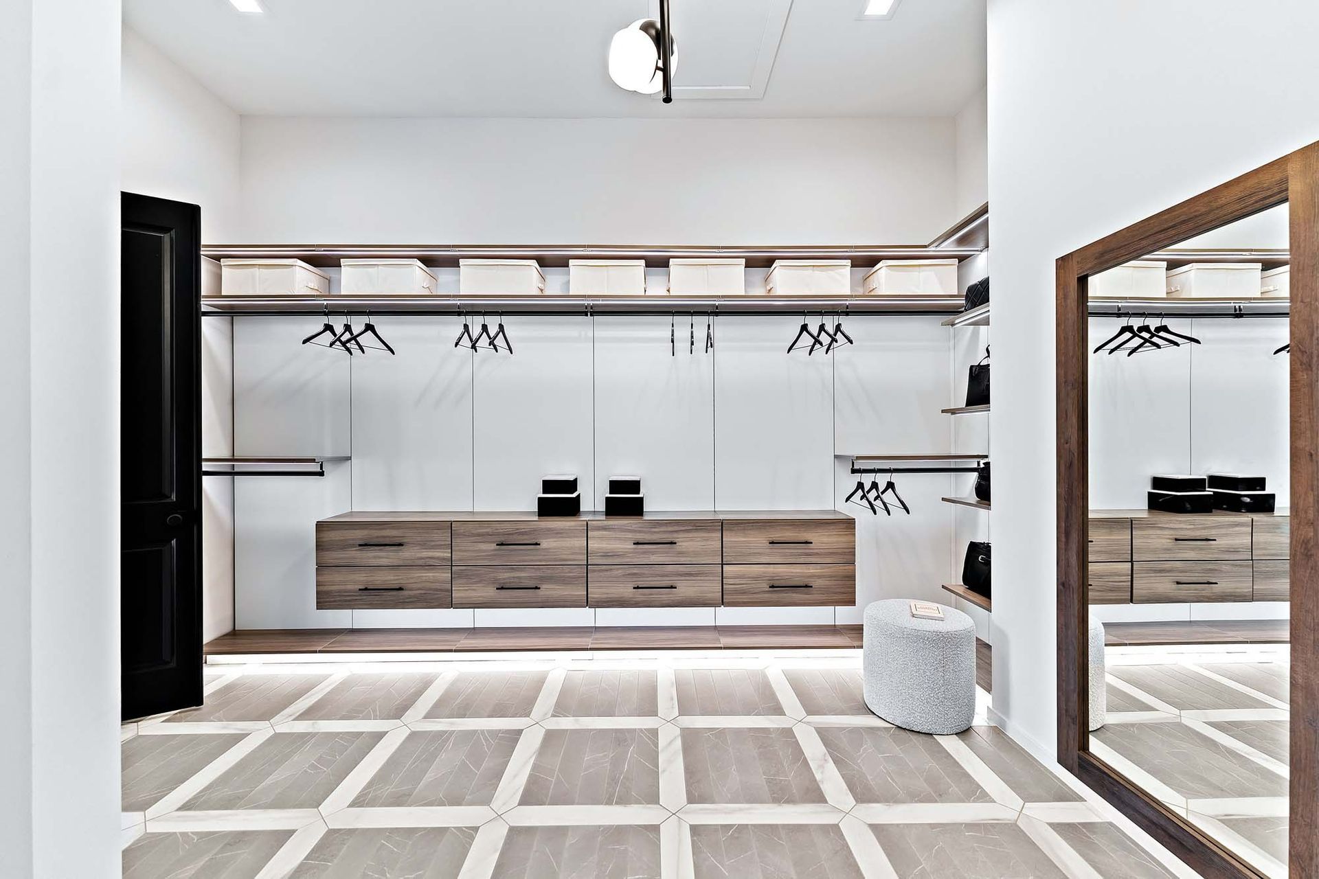 Modern walk-in closet with wood drawers, open shelving, hanging rods, and a large mirror on a white tiled floor