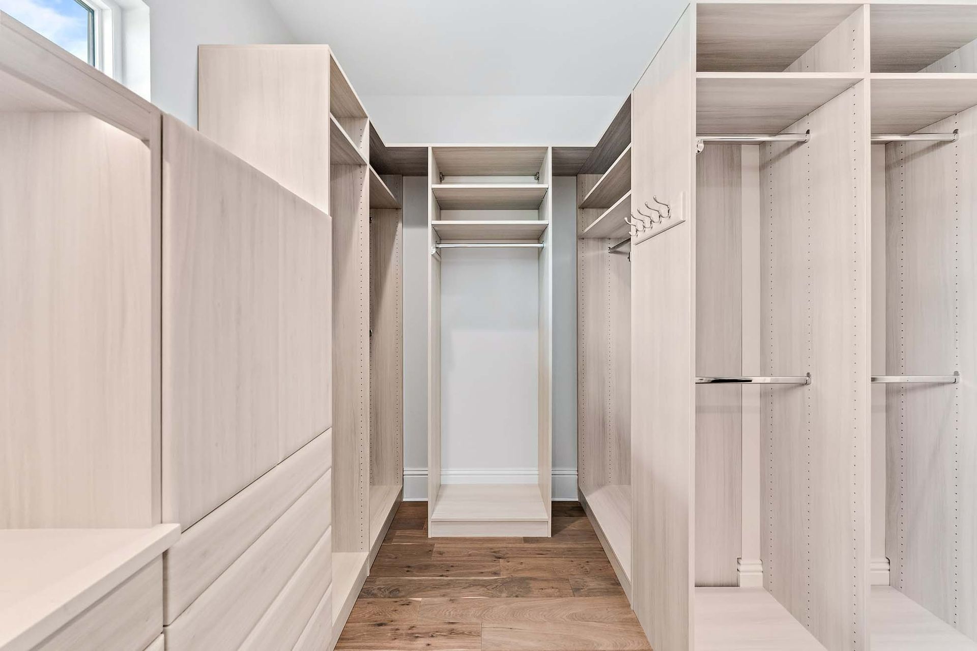 Empty walk-in closet with white shelving, hanging rods, and light wood flooring.