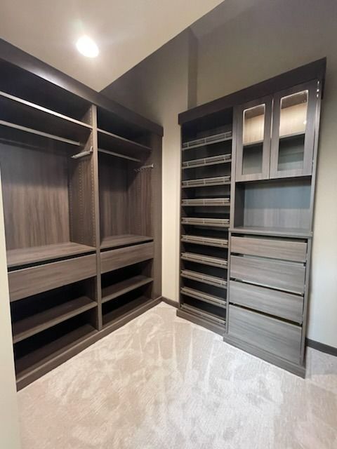 Empty walk-in closet with dark wood shelving, hanging rods, and gray drawers under a ceiling light