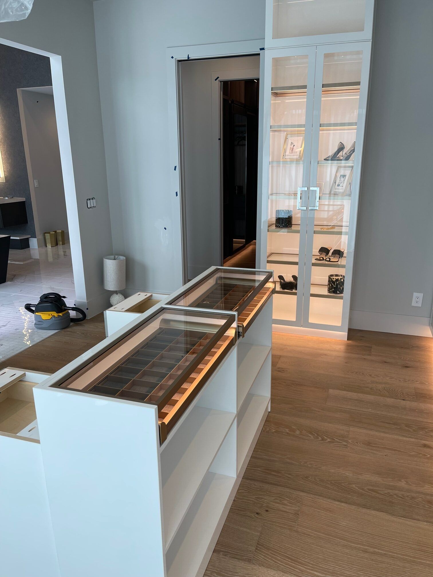 Empty modern room with hardwood floors, white walls, and a glass display cabinet near a doorway.