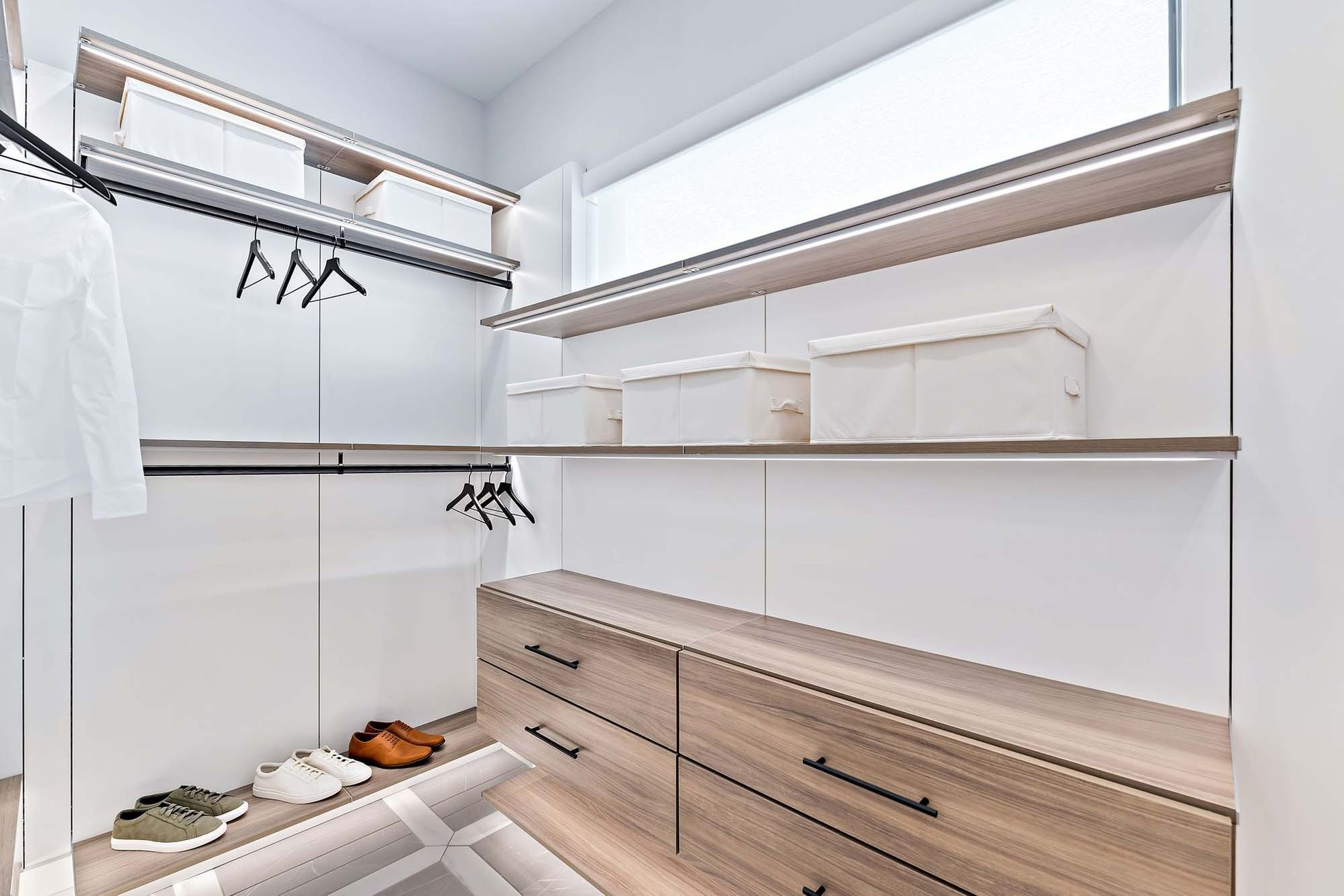 Walk-in closet with white shelving, hanging rods, and light wood drawers