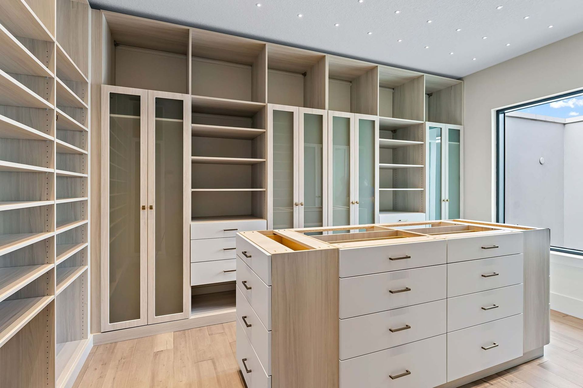 Modern walk-in closet with white built-in shelves, drawers, and an island storage unit.