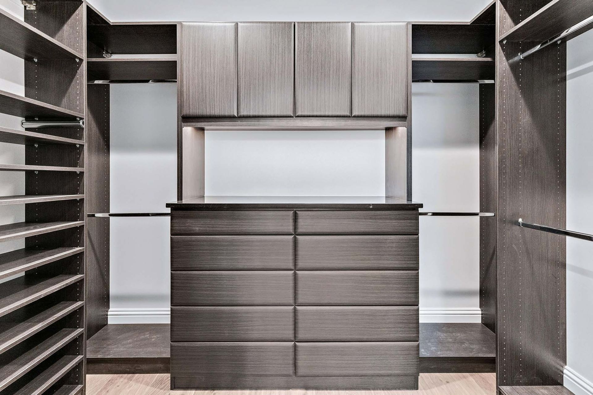 Built-in dark wood closet with drawers, shelves, and a central hanging area in a walk-in wardrobe.