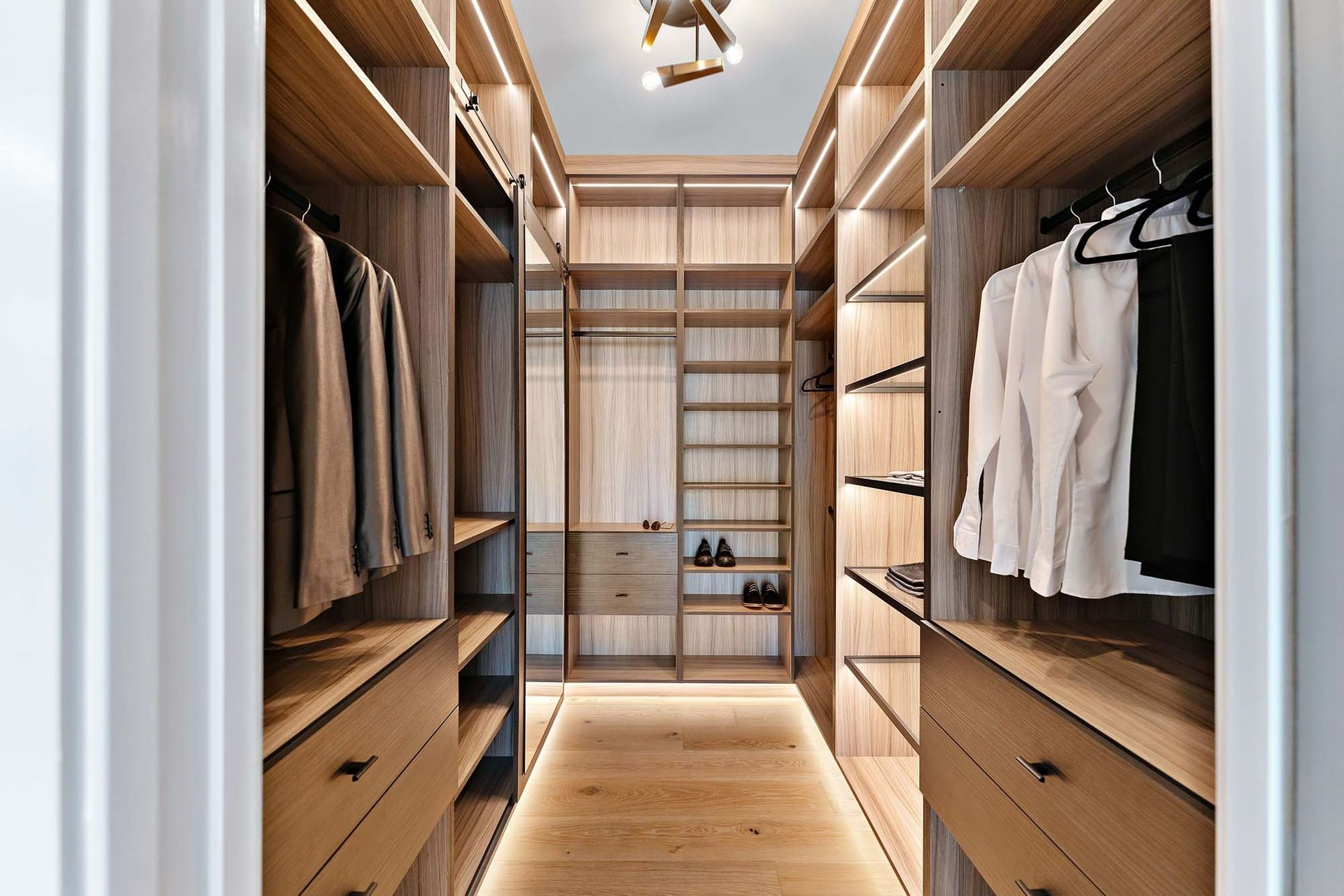 Walk-in closet with wooden shelves, hanging clothes, drawers, and a bench in the center.