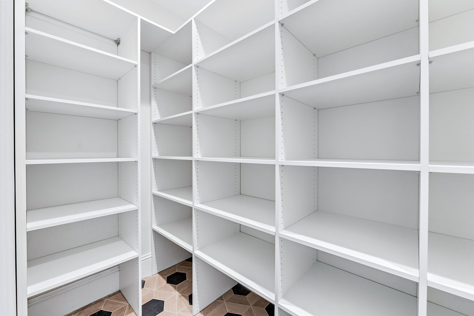 Empty white built-in shelving in a bright closet or storage room, with tiled floor and wood trim.