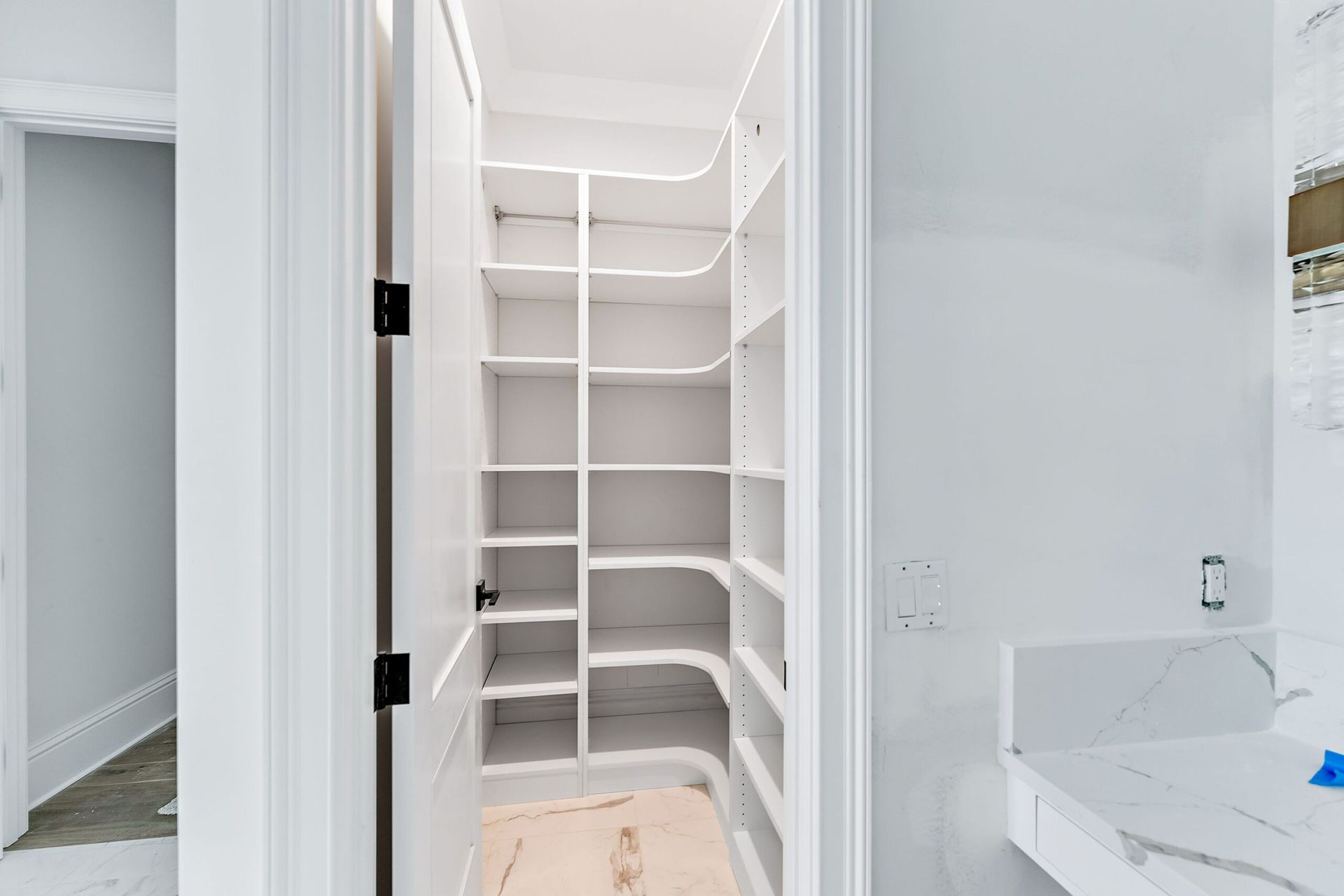 Built-in white shelving in a narrow closet beside a bathroom vanity and doorway