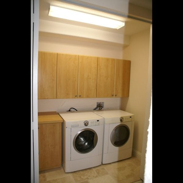 Small laundry room with wood cabinets and two front-loading machines, one washer and one dryer.