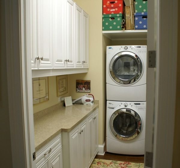 Small laundry room with stacked washer and dryer, white cabinets, and beige counters.