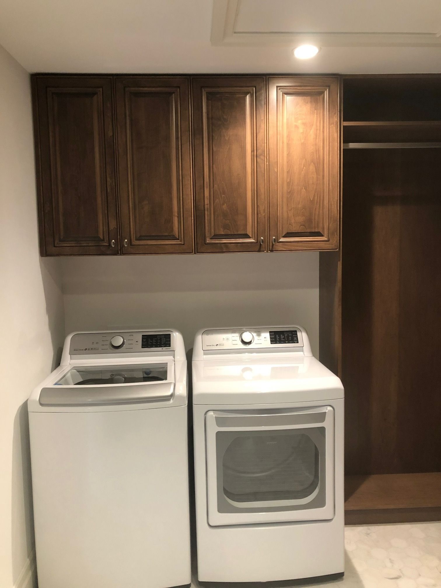 Laundry room with a white washer and dryer beneath dark wood cabinets.