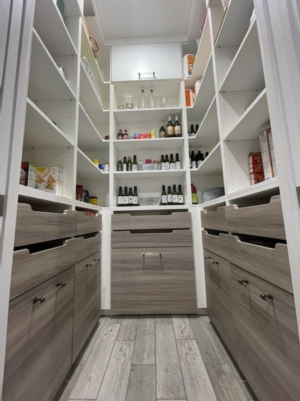Narrow walk-in pantry with white shelves, gray drawers, and assorted bottles and jars.