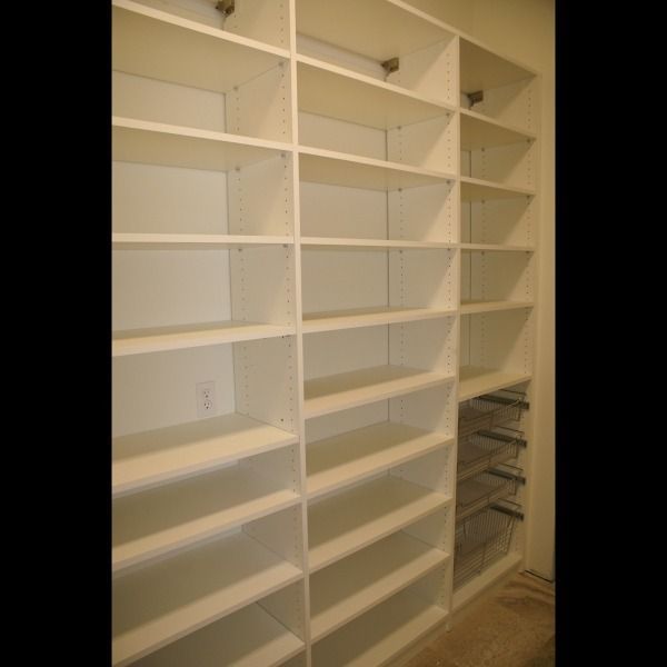 White built-in shelving and cubby shelves in a closet or pantry, with stacked wire baskets on the right.