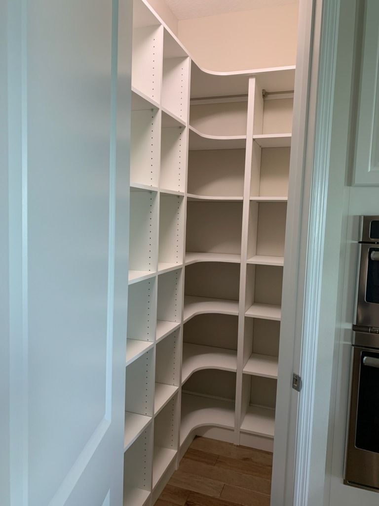 Empty white pantry shelves in a narrow closet with a wood floor